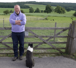 Photo of Rob Nicholson and a sheepdog in front of a farm gate