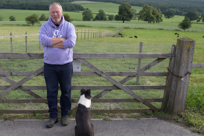 Photo of Rob Nicholson and a sheepdog in front of a farm gate