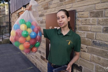 Photo of Kate holding a sack of plastic multi coloured toy balls which will create a ball-pit for the meerkats