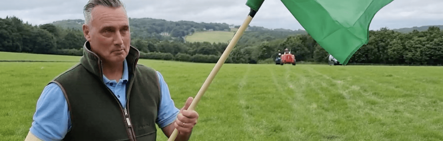 Photo of farmer David Nicholson holding a flag in a field with a tractor in the distance