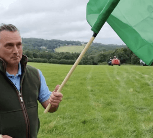 Photo of farmer David Nicholson holding a flag in a field with a tractor in the distance