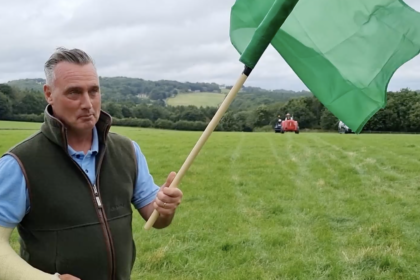 Photo of farmer David Nicholson holding a flag in a field with a tractor in the distance